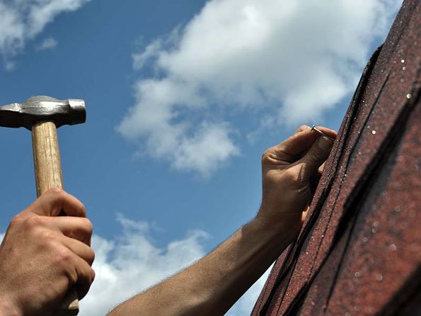 Hammer schlägt Nagel in Dachpappe